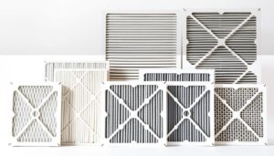 A detailed, high-resolution image of seven common types of HVAC air filters, presented in a clean, organized layout. The filters are shown in a well-lit, neutral studio setting, with soft, directional lighting that highlights their textures and materials. The filters are arranged in a row, with each type clearly visible and distinct. The background is a simple, uncluttered white or light gray, allowing the filters to be the focal point. The image conveys a sense of technical precision and visual clarity, suitable for an informative article on HVAC air filter selection.